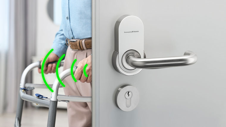 Persona anziana utilizza un deambulatore mentre apre una porta con maniglia intelligente seamless SimonsVoss, evidenziata da segnali wireless.