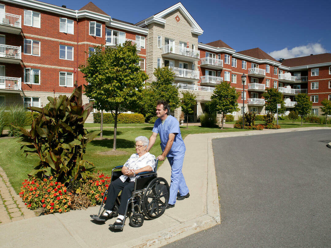 Pfleger mit Patientin im Rollstuhl vor Senioreneinrichtung